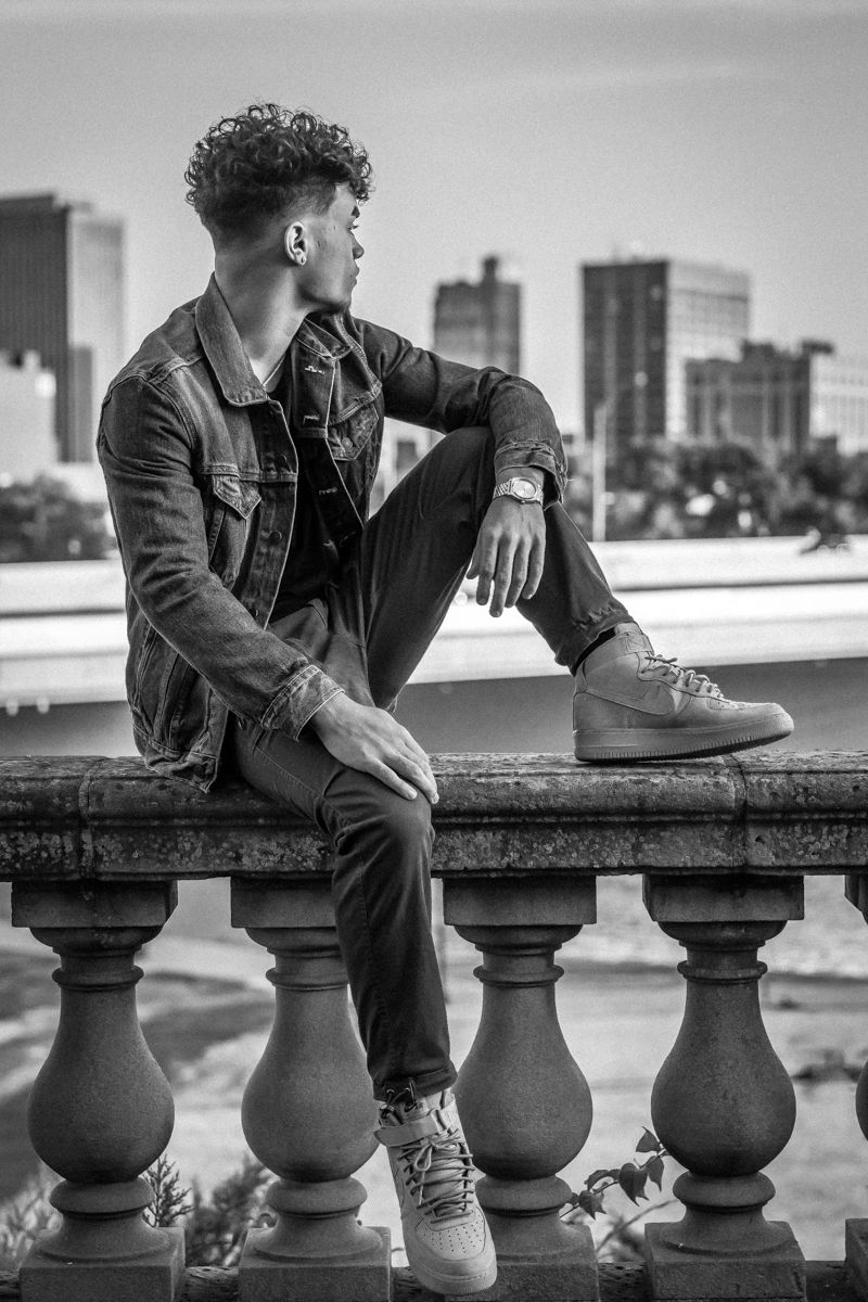 Black and white portrait of a senior seated on a stone balustrade, looking out over the Dayton skyline